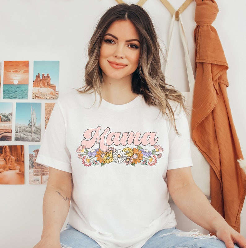 Puede incluir: Camiseta blanca con un gr&aacute;fico rosa de "Mama" y un dise&ntilde;o floral. Las flores son en tonos de amarillo, naranja, rosa y morado.