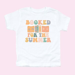May include: White t-shirt with a colorful graphic that says "BOOKED FOR THE SUMMER" with a stack of books in the middle of the text.