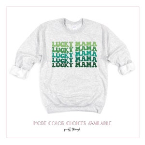 May include: A gray sweatshirt with the text "LUCKY MAMA" repeated five times in a green, blue, and white gradient. The text is in a retro font style.