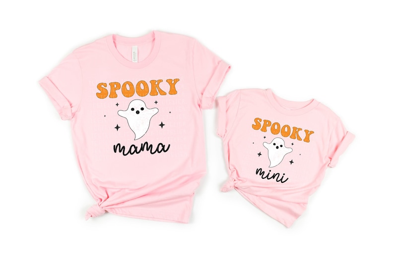 K&ouml;nnte beinhalten: Zwei rosa T-Shirts mit einem Geistermotiv und dem Text "Spooky mama" und "Spooky mini" in orangefarbenen Buchstaben.