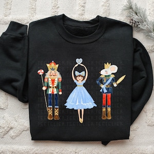 May include: Black sweatshirt featuring a watercolor illustration of three characters from The Nutcracker ballet. The characters include a nutcracker, a ballerina, and a mouse king. The nutcracker holds a candy cane, and the ballerina holds a heart.