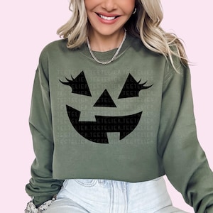 a woman wearing a green sweatshirt with a black pumpkin face on it