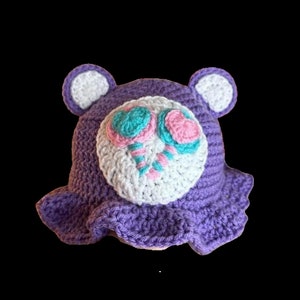 May include: Purple crocheted sun hat with floppy brim and two white crocheted candy cane designs on the front.