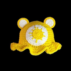May include: Yellow crocheted sun hat with white crocheted sun design. The hat has a wide brim and ear flaps.