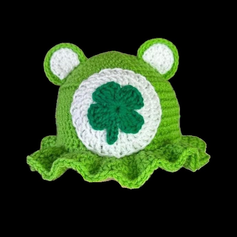 May include: Green crocheted hat with a white clover design. The hat has a ruffled brim.