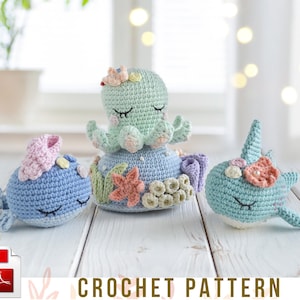May include: Three crocheted sea creatures: a blue whale, a green octopus, and a blue whale with a horn. Each has closed eyes and decorative accents. The text "CROCHET PATTERN" is displayed below the toys.