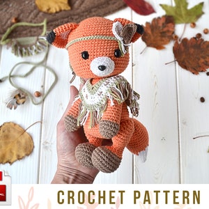 May include: Crochet pattern for a cute orange fox amigurumi toy with a brown and white fringed scarf. The fox has a brown nose, black eyes, and a small brown feather on its head.