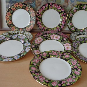 May include: Set of eight floral patterned dessert plates with gold trim. The plates feature a black background with colourful flowers and gold accents.