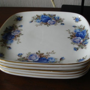 Peut inclure: Un ensemble de quatre assiettes carrées en céramique avec un bord doré et un motif de roses bleues.