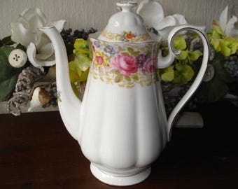 Pode incluir: Bule de porcelana branca com um design floral em tons de rosa, roxo e amarelo. A chaleira tem uma tampa e uma alça.