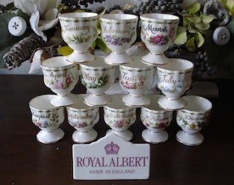 Puede incluir: Un juego de 12 hueveras Royal Albert, cada una decorada con un mes diferente del año y diseños florales. Las hueveras están apiladas en forma de pirámide, con el logotipo de Royal Albert y el texto "Made in England" en un pequeño cartel delante.