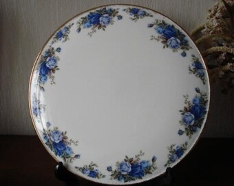May include: A white ceramic cake plate with a gold rim and a blue and white floral design. The plate is on a black stand.