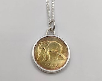 Könnte beinhalten: Eine silberne Kettenkette mit einem goldfarbenen Anhänger mit einem Elefantenmotiv und dem Jahr 1946.