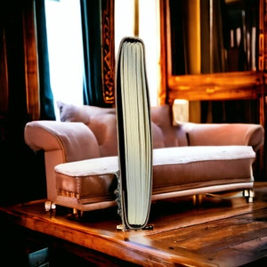Puede incluir: Un libro grueso, blanco y encuadernado, de pie sobre una mesa de madera. El libro est&aacute; delante de un sof&aacute; marr&oacute;n claro con un coj&iacute;n blanco.