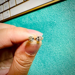 May include: A pair of small, round, silver stud earrings with a cluster of clear, sparkling stones.