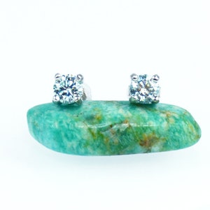 May include: A pair of silver stud earrings with clear round gemstones set in a four-prong setting.