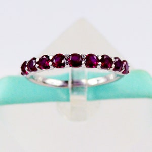 May include: A silver band ring with a row of deep red ruby stones.