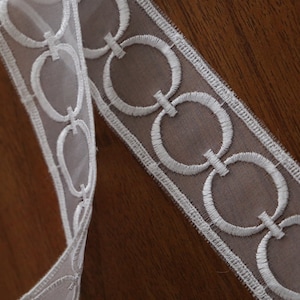 May include: White sheer ribbon with a white embroidered design of interlocking circles.