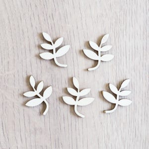 Peut inclure: Six formes de feuilles en bois blanc, chacune avec un design diff&eacute;rent, sont dispos&eacute;es sur une surface en bois clair.