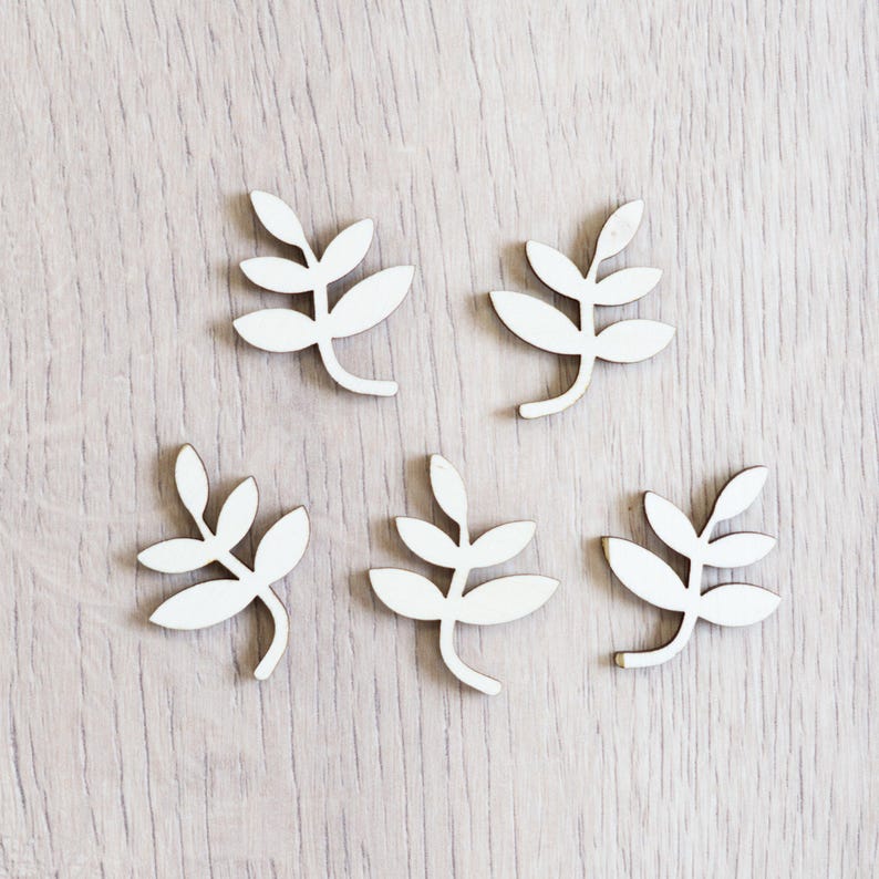 Peut inclure: Six formes de feuilles en bois blanc, chacune avec un design diff&eacute;rent, sont dispos&eacute;es sur une surface en bois clair.