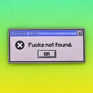 以下が含まれることがあります： コンピューターのエラーメッセージボックスの形をしたシルバーカラーのピン。上部に「Error 404」、下に「Fucks not found.」と「OK」ボタンと書かれています。背景は緑と黄色のグラデーションです。