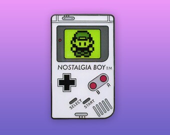 May include: A white and gray enamel pin shaped like a handheld video game console. The screen displays a pixelated green character. The console has the text "NOSTALGIA BOY™" printed on the front.