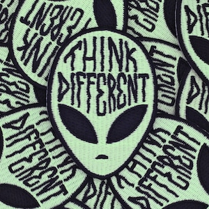 May include: A close-up of several green and black embroidered patches with an alien head and the text "Think Different".