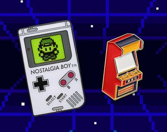 May include: Two enamel pins depicting retro video game consoles. The first pin is white and features a pixelated image of a video game character on a green screen. The pin reads "NOSTALGIA BOY TM". The second pin is red and features a pixelated arcade cabinet with a black screen.