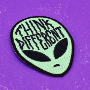 May include: Green alien-shaped embroidered patch with black stitching. The patch says "Think Different" in a black cursive font.