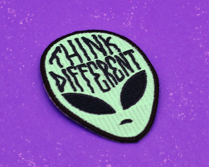 May include: Green alien-shaped embroidered patch with black stitching. The patch says "Think Different" in a black cursive font.