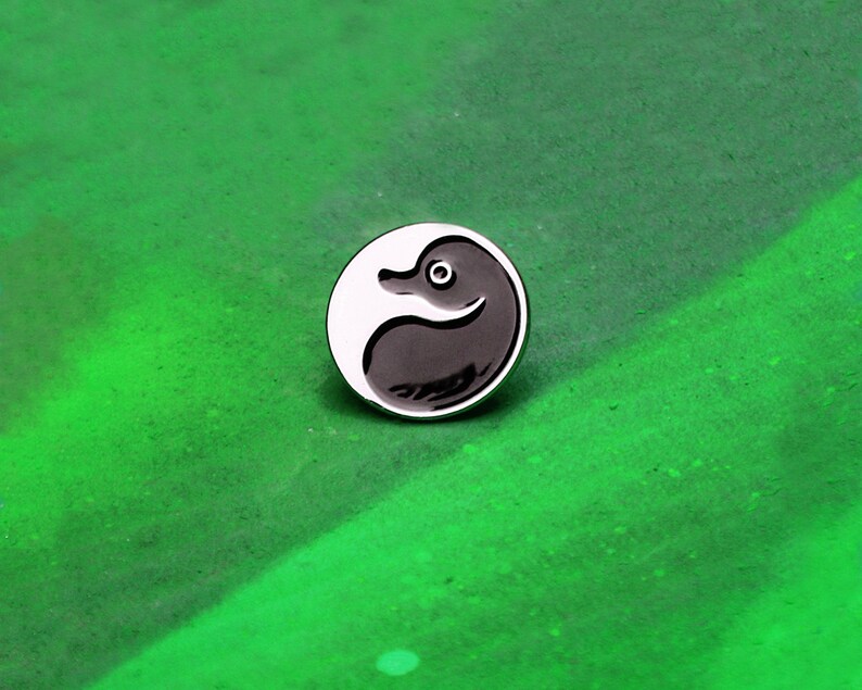 May include: A black and white enamel pin featuring a stylized duck in a yin yang design.