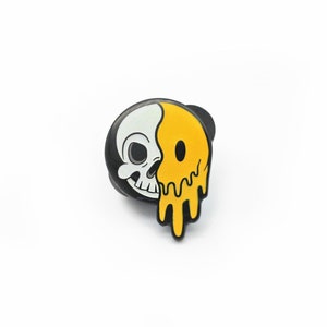 May include: A black and white skull and yellow smiley face enamel pin. The pin features a half skull and half melting smiley face design. The pin is a fun accessory for jackets, bags, or hats.