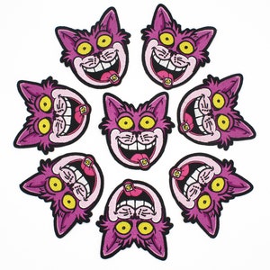 K&ouml;nnte beinhalten: Acht gestickte Aufn&auml;her mit einem Cartoon-Katzenkopf mit breitem Grinsen und herausgestreckter Zunge. Die Katze ist rosa mit gelben Augen und schwarzer Umrandung. Die Aufn&auml;her sind kreisf&ouml;rmig auf wei&szlig;em Hintergrund angeordnet.