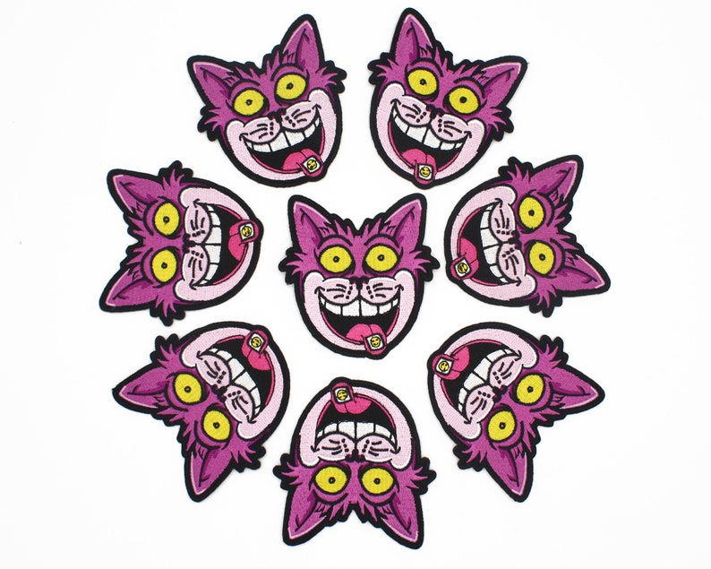 K&ouml;nnte beinhalten: Acht gestickte Aufn&auml;her mit einem Cartoon-Katzenkopf mit breitem Grinsen und herausgestreckter Zunge. Die Katze ist rosa mit gelben Augen und schwarzer Umrandung. Die Aufn&auml;her sind kreisf&ouml;rmig auf wei&szlig;em Hintergrund angeordnet.