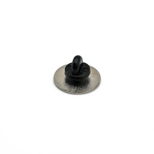 May include: The back of a silver pin with a black metal clasp.
