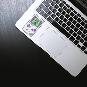 May include: A silver laptop computer with a black keyboard and a sticker of a retro video game console with the text "NOSTALGIA BOY" on the top of the trackpad.