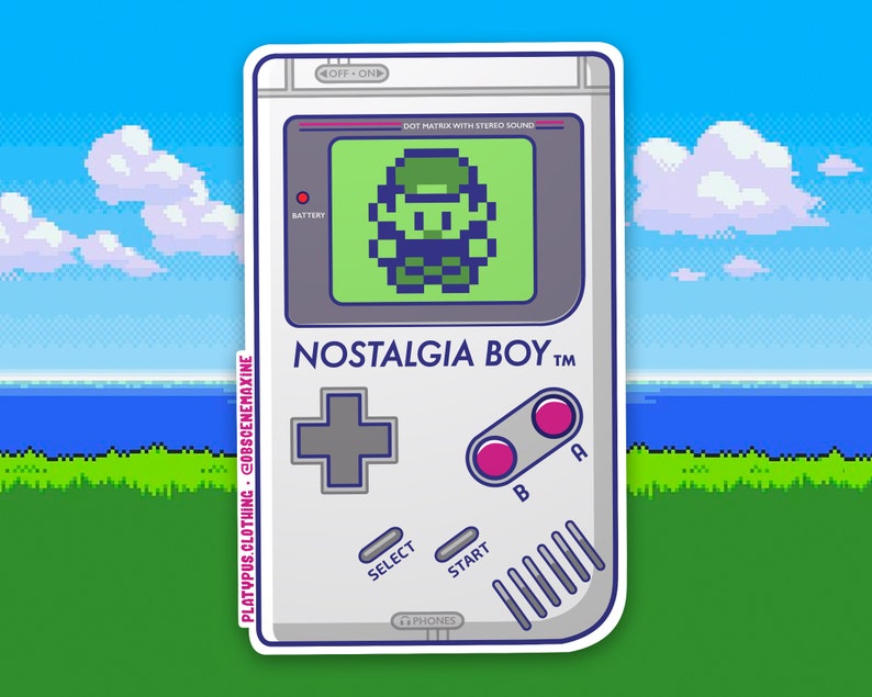 May include: A white and gray handheld video game console with a green screen displaying a pixelated character. The console has a gray plus sign button, two pink buttons labeled "A" and "B", a "SELECT" button, a "START" button, and the text "NOSTALGIA BOY TM".