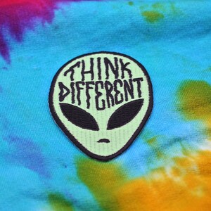 May include: Green alien head embroidered patch with the text "Think Different" in black.