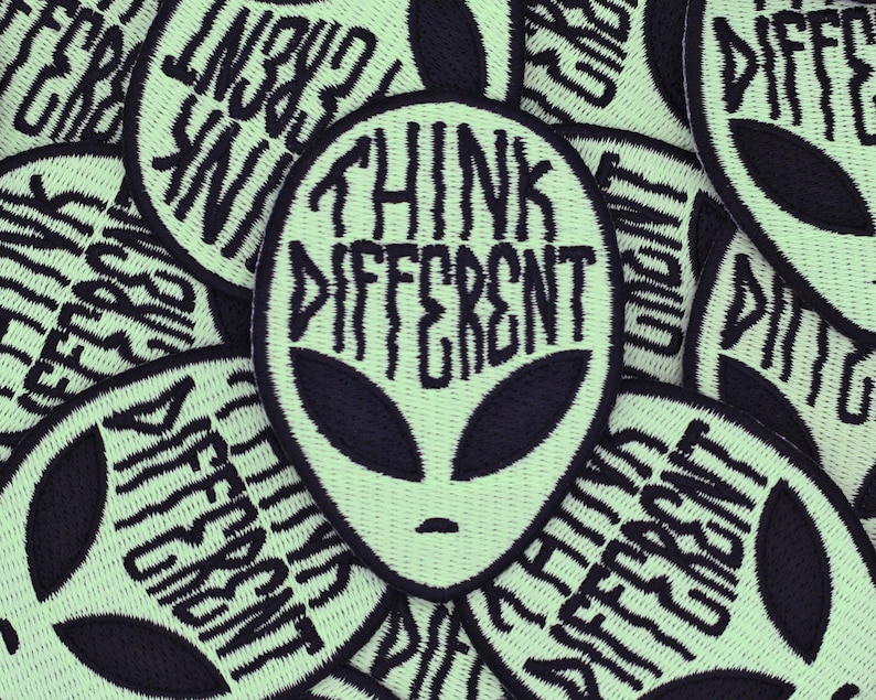 May include: A close-up of several green and black embroidered patches with an alien head and the text "Think Different".