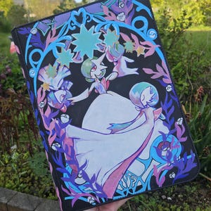 Op de afbeelding: Zwarte etui met een kleurrijke illustratie van een personage in een witte jurk en groen haar, omringd door blauwe, paarse en roze bloemen- en stermotieven. De etui heeft een zwarte rand.