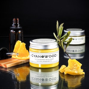 K&ouml;nnte beinhalten: Ein kleines Glas mit gelber Holzpolitur und einem silbernen Deckel. Das Glas ist mit "CYANWOOD - CUTTING BOARD WOOD FINISH - NATURAL INGREDIENTS" beschriftet. Im Hintergrund sind Orangenscheiben und eine Tropfflasche zu sehen.