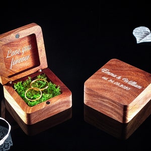 Könnte beinhalten: Eine Holz-Ringbox mit der Gravur "Love you forever" im Inneren. Zwei goldene Ringe liegen auf grünem Moos. Eine zweite Box ist mit "Emma & William est. 24.09.2020" graviert.