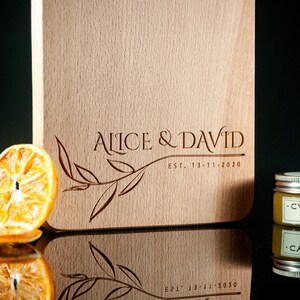 May include: A wooden chopping board with the text "Alice & David Est. 13-11-2020" engraved on it. A small jar of wood conditioner is in the foreground.