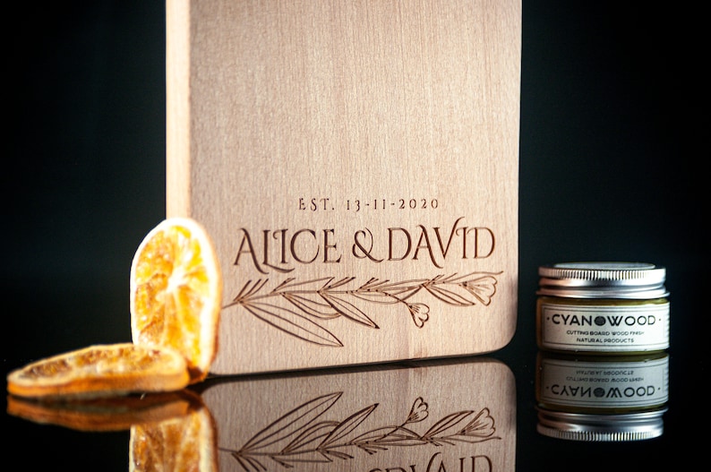 K&ouml;nnte beinhalten: Ein Schneidebrett aus Holz mit dem eingravierten Text "EST. 13-11-2020 ALICE & DAVID". Das Brett ist mit einem floralen Design verziert und hat eine nat&uuml;rliche Holzoptik.