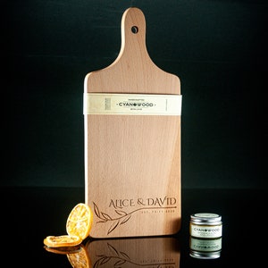 May include: A personalised wooden chopping board with a handle, engraved with the text "Alice & David Est. 12-11-2020" and a leafy design. The board is made by Cyanwood.