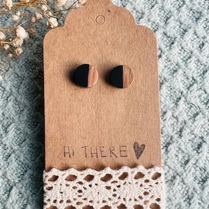 May include: A pair of wooden earrings with a black and wood grain design. The earrings are displayed on a brown card with the text "Hi There" and a heart.
