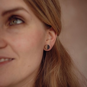 May include: A close-up of a person's ear wearing a pair of round wooden earrings. The earrings are half black and half wood.