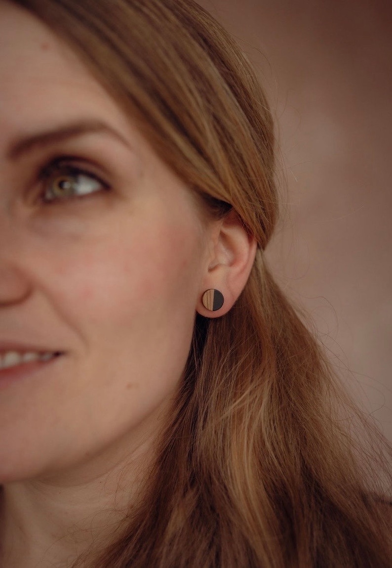 May include: A close-up of a person's ear wearing a pair of round wooden earrings. The earrings are half black and half wood.