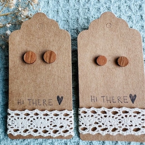 Könnte beinhalten: Zwei Paar Holzohrringe auf braunem Karton mit dem Text "Hi There" und einem Herz. Die Ohrringe sind rund und braun.