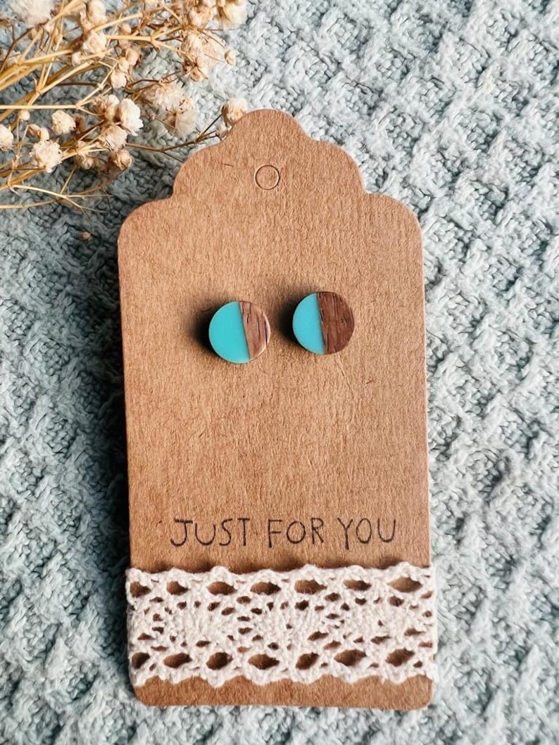 May include: A pair of turquoise and brown wood earrings. The earrings are round and have a half-circle of turquoise resin on top of the wood. The earrings are on a brown card with the text "JUST FOR YOU".